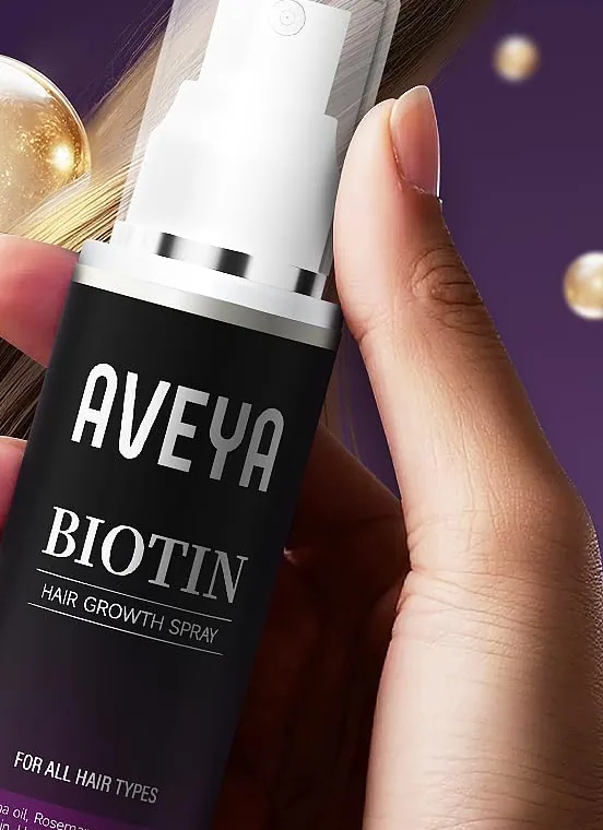 The AVEYA Biotin Hair Growth Spray bottle held in a hand